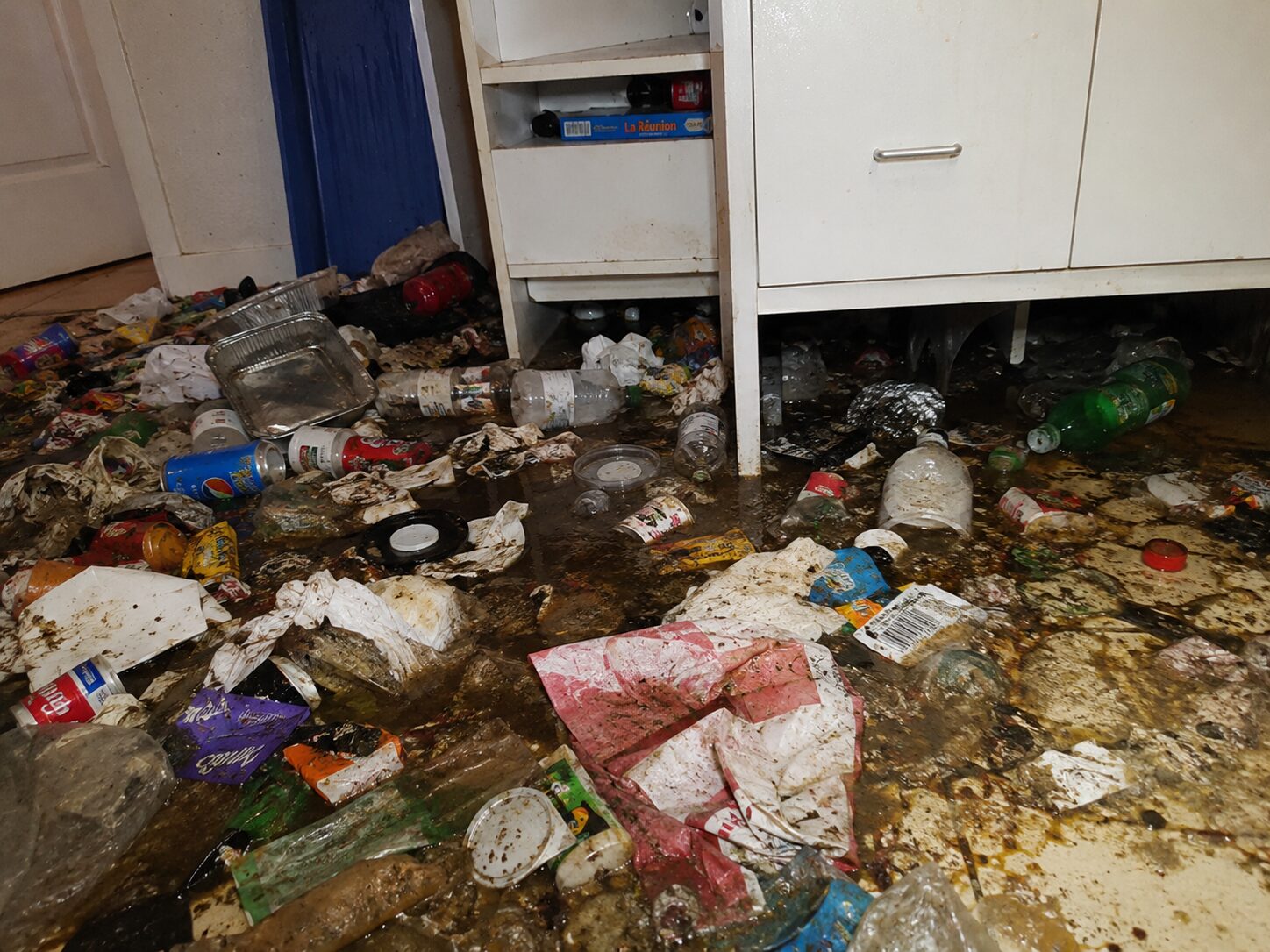 Sol très sale avec déchets, liquides de poubelle et résidus ayant coulé sous les meubles d’un logement à nettoyer