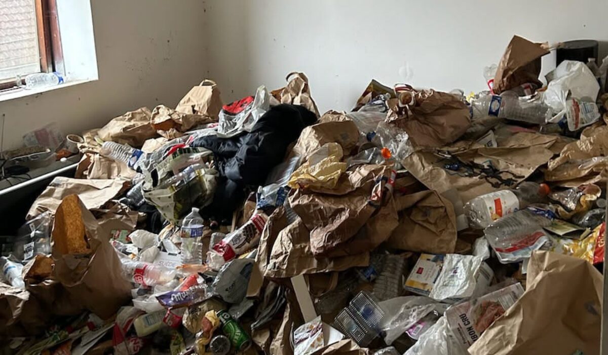 Pièce très encombrée avec accumulation de sacs en papier, bouteilles plastiques, emballages et déchets au sol, dans un contexte de logement insalubre suite à un syndrome de diogène