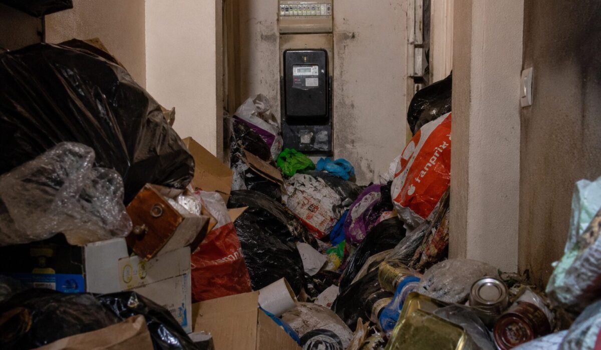 Logement très encombré avec un compteur électrique difficile d’accès derrière des déchets, sacs-poubelle et cartons