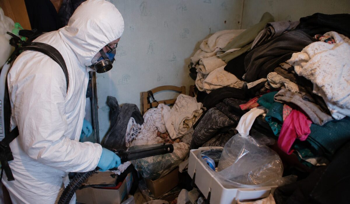 Technicien traitant une infestation de mites textiles dans une pièce encombrée de vêtements et de textiles