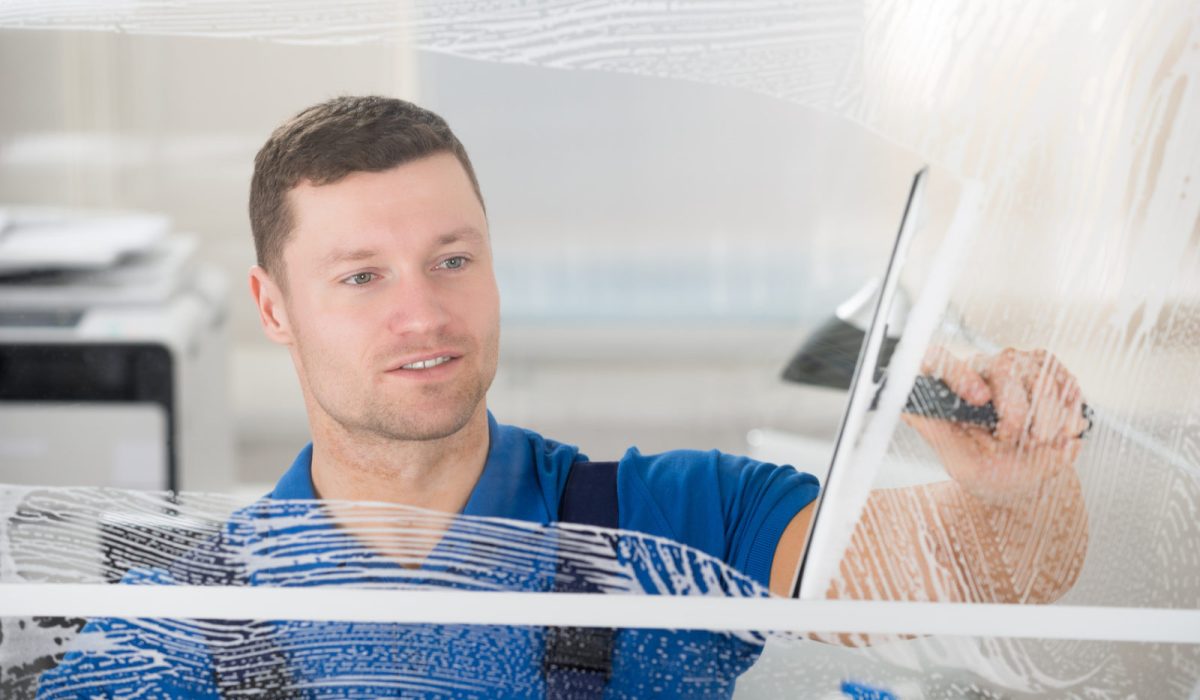 Smiling mid adult worker cleaning soap sud on glass window with squeegee