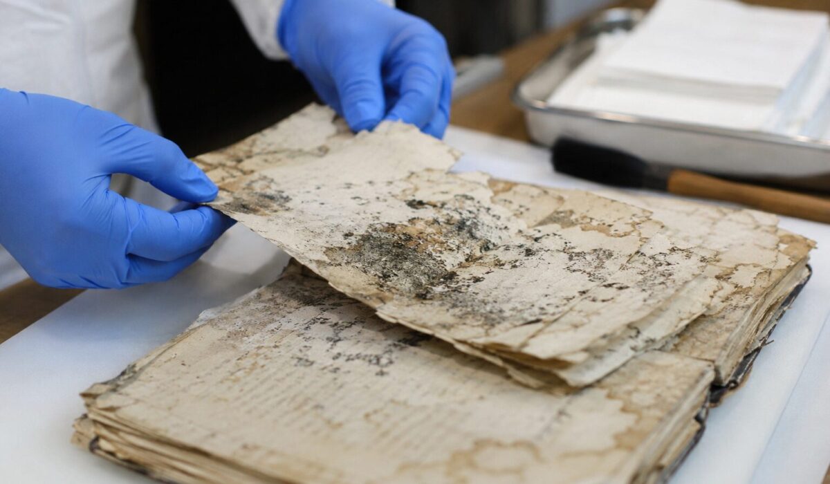 Archiviste manipulant avec précaution des papiers moisis et collés pour préserver des documents anciens sans les détruire
