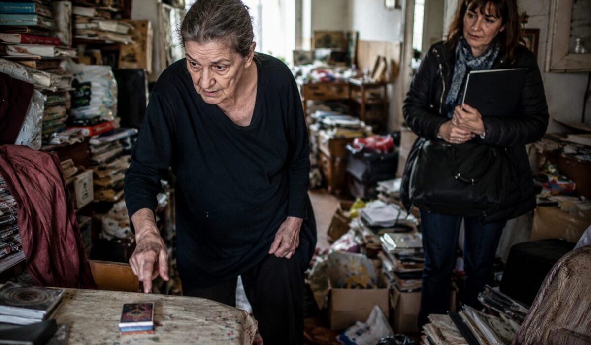 Patient en incurie inquiet face à un objet déplacé dans un logement très encombré accompagné par une intervenante sociale