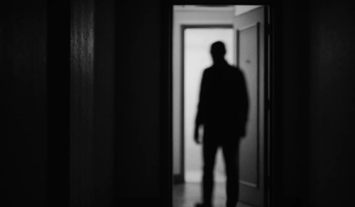 Silhouette floue d'une personne devant une porte, couloir sombre, noir et blanc