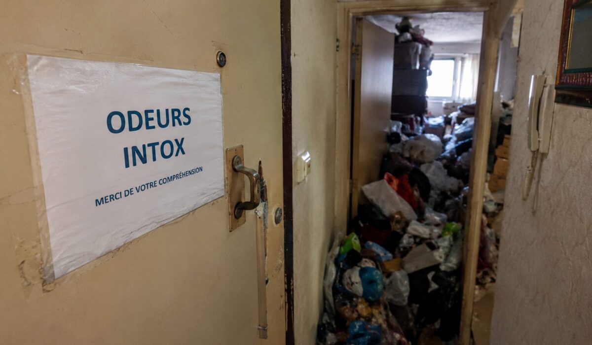 Cage d’escalier d’immeuble avec porte ouverte sur un logement très encombré provoquant des odeurs fortes dans les parties communes