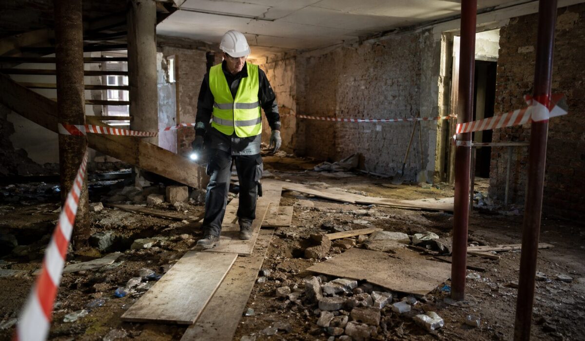 Professionnel équipé sécurisant un sol instable recouvert de déchets, gravats, clous et verre dans un chantier balisé