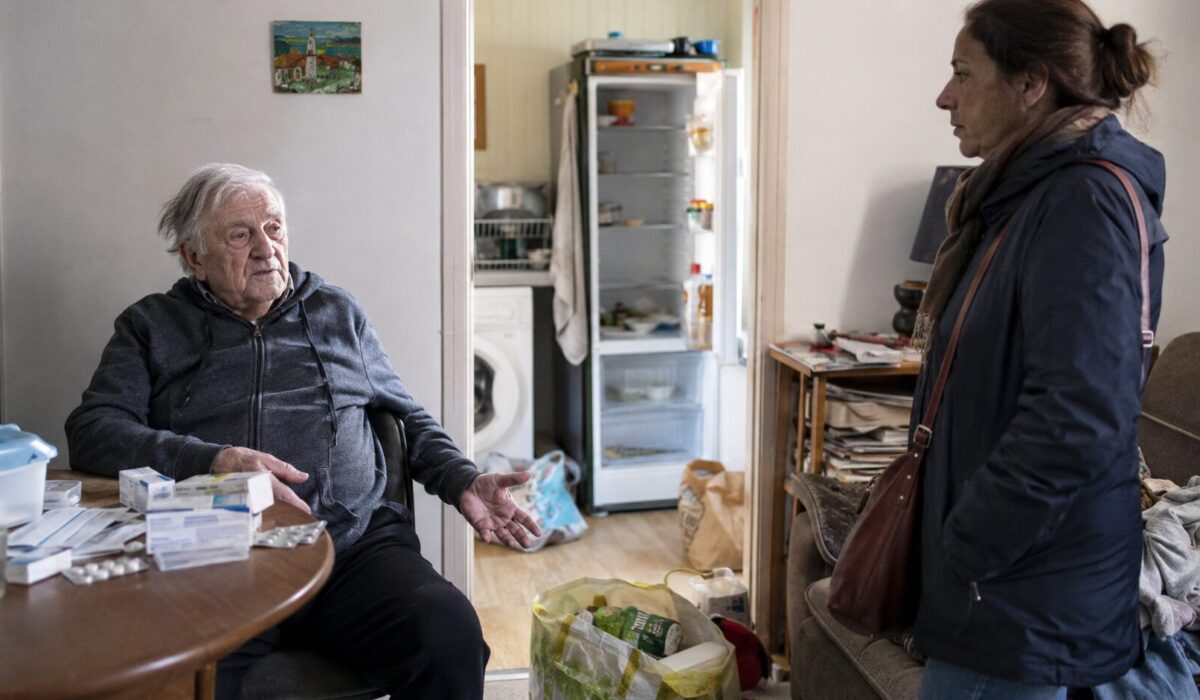 Patient âgé en situation d’incurie dans un logement encombré face à une aidante attentive, avec signes d’alerte visibles comme médicaments, courrier et réfrigérateur presque vide